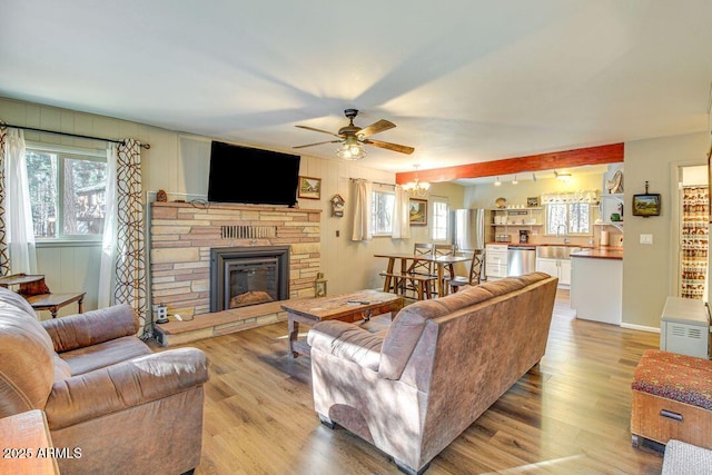 living room featuring ceiling fan with notable chandelier, a stone fireplace, wood finished floors, and a healthy amount of sunlight