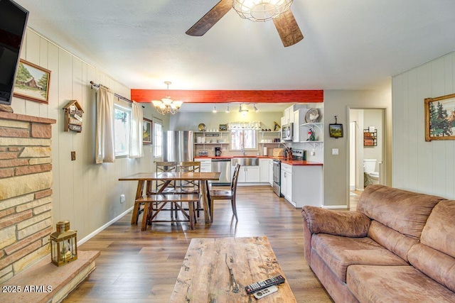 living room featuring baseboards, wood finished floors, and ceiling fan with notable chandelier