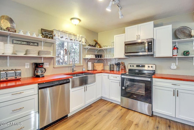 kitchen with appliances with stainless steel finishes, wooden counters, a sink, and open shelves