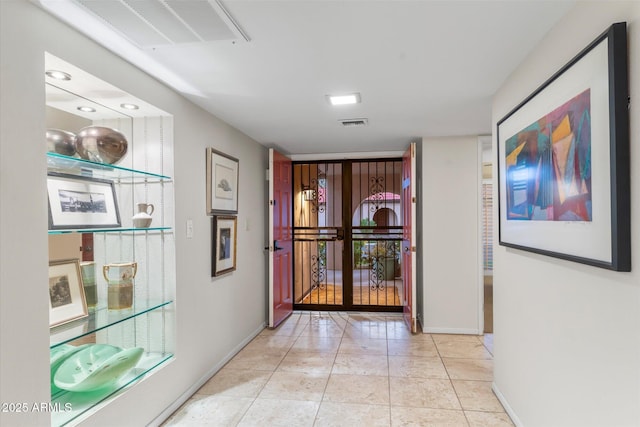 hall featuring visible vents, baseboards, and light tile patterned floors