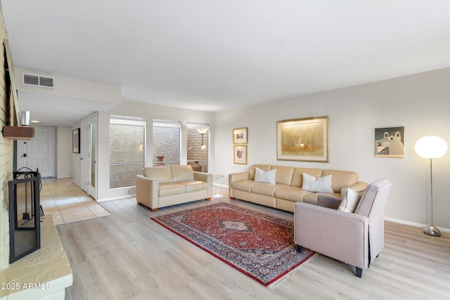 living area featuring light wood-style floors, baseboards, visible vents, and a fireplace with raised hearth