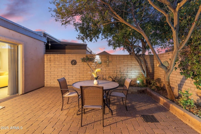 patio terrace at dusk featuring outdoor dining space, a fenced backyard, and visible vents