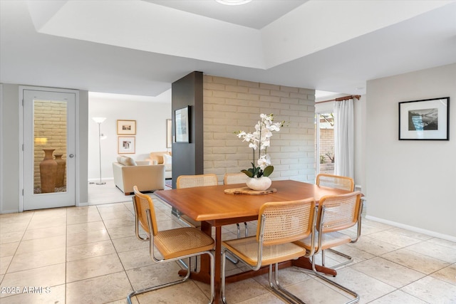 dining space featuring brick wall, light tile patterned flooring, and baseboards