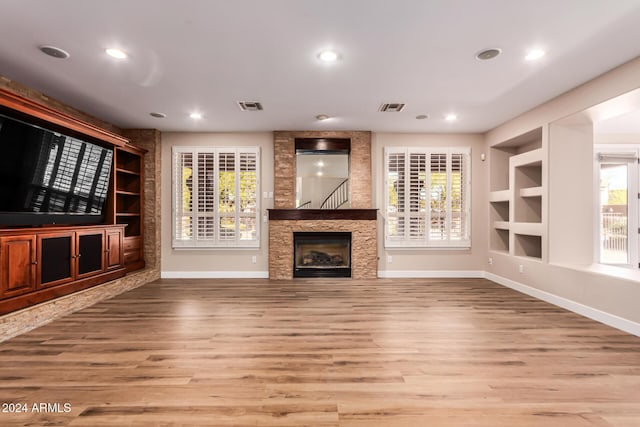 unfurnished living room featuring a fireplace, plenty of natural light, light hardwood / wood-style floors, and built in shelves