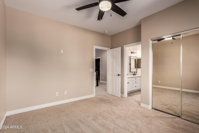 unfurnished bedroom featuring light carpet, ensuite bathroom, sink, ceiling fan, and a closet