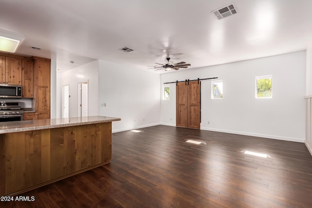 kitchen featuring light stone countertops, appliances with stainless steel finishes, ceiling fan, a barn door, and dark hardwood / wood-style floors