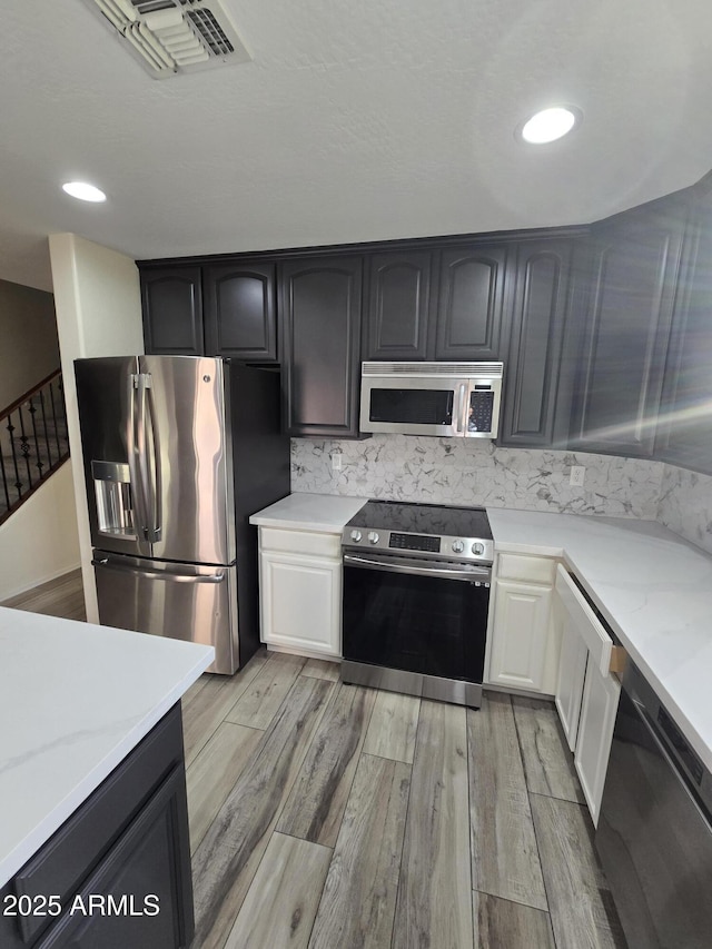 kitchen featuring light wood finished floors, white cabinetry, stainless steel appliances, and light stone counters