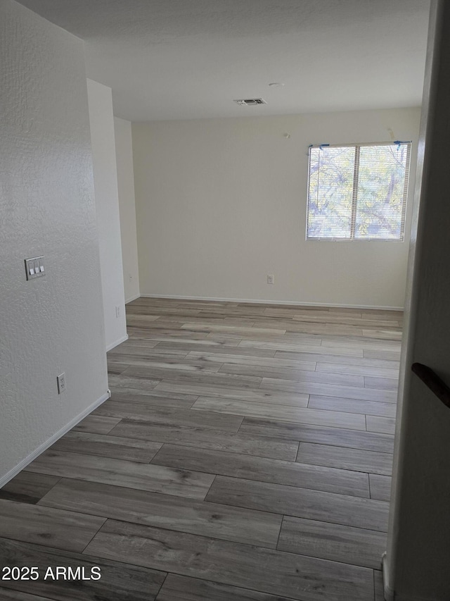 empty room featuring a textured wall, visible vents, baseboards, and wood finished floors