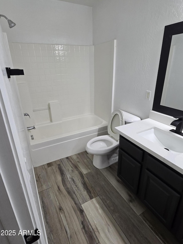 bathroom with toilet, shower / washtub combination, wood finished floors, vanity, and a textured wall