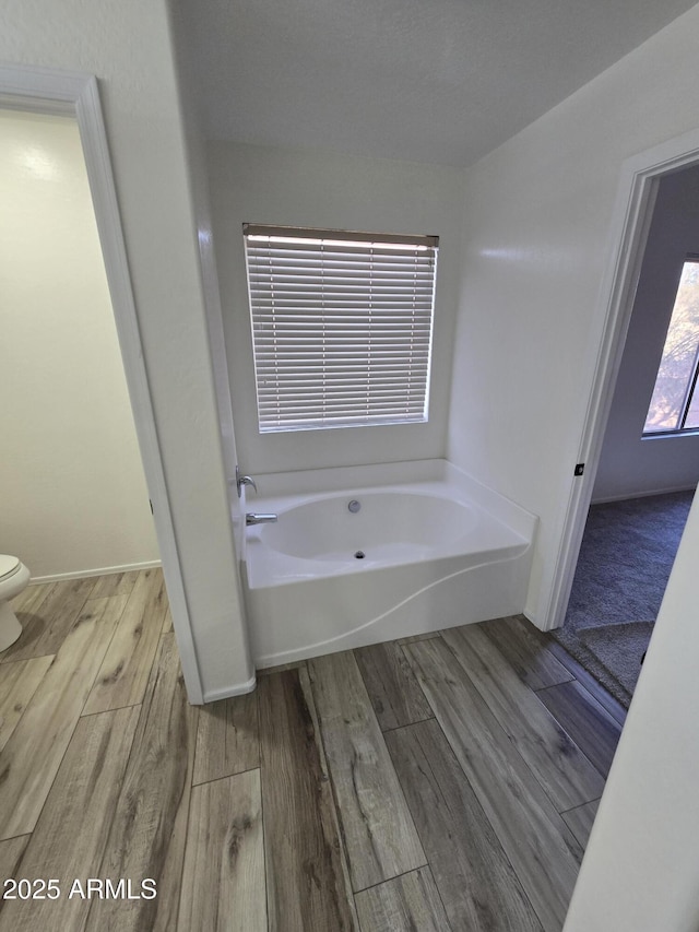 bathroom featuring a bath, toilet, baseboards, and wood finished floors