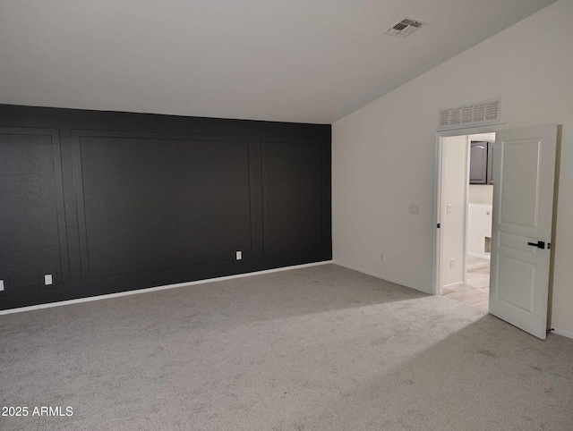 empty room featuring light carpet, visible vents, and vaulted ceiling