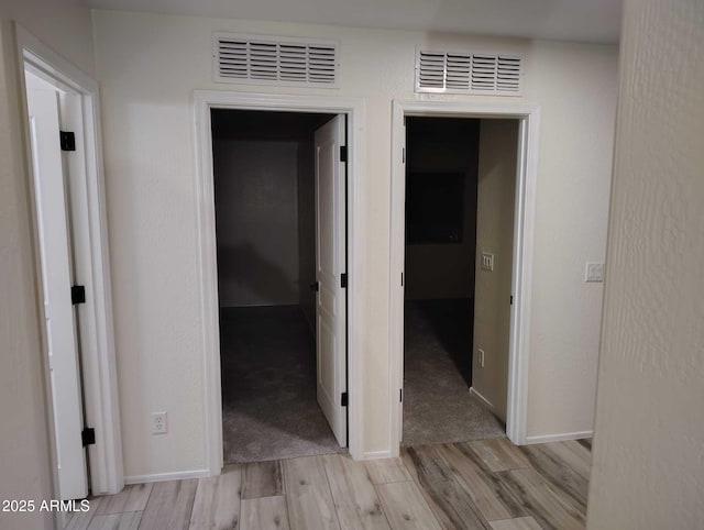 corridor featuring light wood finished floors, visible vents, and baseboards