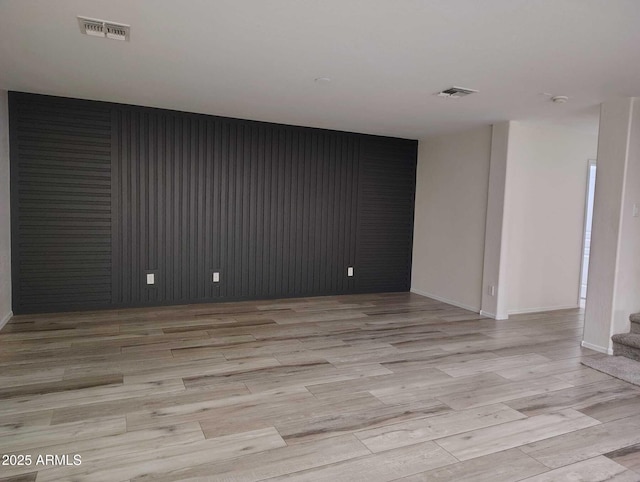 spare room with stairs, light wood-style floors, visible vents, and baseboards