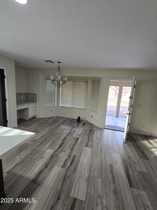 unfurnished living room with an inviting chandelier, wood finished floors, and visible vents