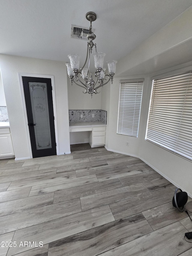 unfurnished dining area featuring visible vents, baseboards, a chandelier, and wood tiled floor