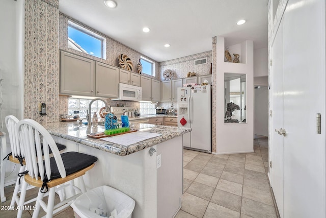 kitchen featuring a breakfast bar, decorative backsplash, kitchen peninsula, light stone countertops, and white appliances