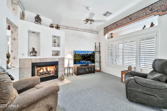 carpeted living room featuring ceiling fan and a tiled fireplace