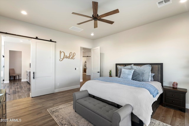 bedroom with ceiling fan, a barn door, and dark hardwood / wood-style floors