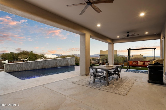 patio terrace at dusk featuring area for grilling, ceiling fan, and pool water feature