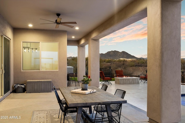 patio terrace at dusk with ceiling fan, a mountain view, and a fire pit