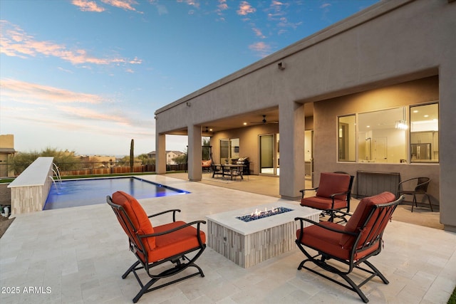 patio terrace at dusk featuring ceiling fan, a fenced in pool, a fire pit, and pool water feature