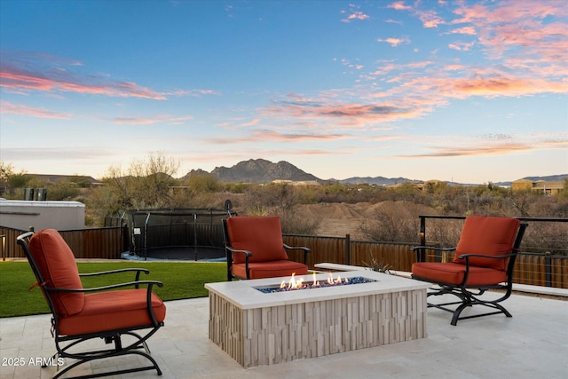 patio terrace at dusk featuring a trampoline, a mountain view, and a fire pit