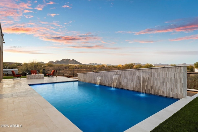 pool at dusk featuring pool water feature, a mountain view, and a patio