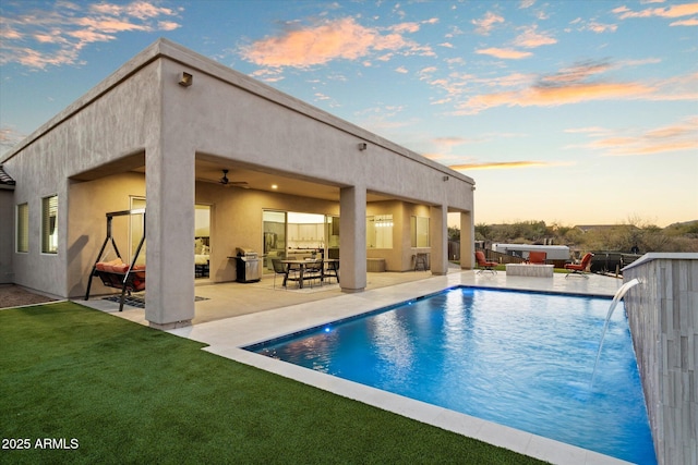 pool at dusk with an outdoor hangout area, pool water feature, ceiling fan, and a patio