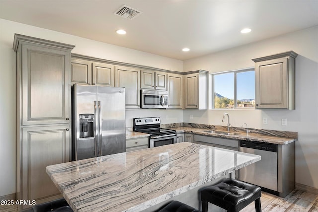 kitchen with a kitchen bar, appliances with stainless steel finishes, sink, light stone counters, and a center island