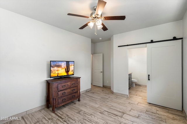 bedroom featuring ceiling fan, light hardwood / wood-style floors, ensuite bathroom, and a barn door