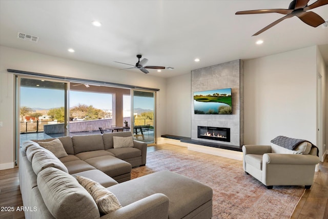 living room with ceiling fan, light hardwood / wood-style flooring, and a tiled fireplace