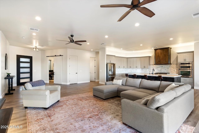 living room with light hardwood / wood-style floors, ceiling fan, sink, and a barn door