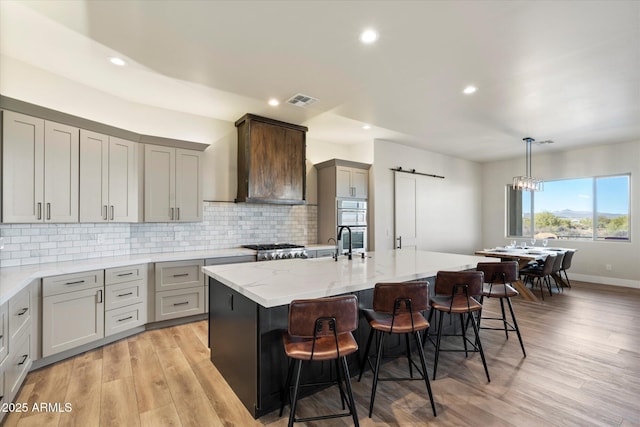 kitchen with decorative light fixtures, light hardwood / wood-style floors, a center island with sink, a breakfast bar, and wall chimney exhaust hood