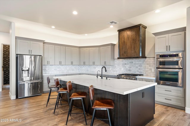 kitchen with a center island with sink, stainless steel appliances, light wood-type flooring, light stone counters, and a breakfast bar