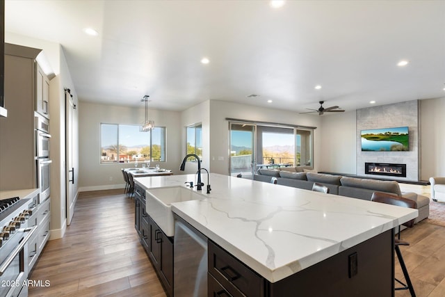 kitchen featuring decorative light fixtures, ceiling fan, sink, light wood-type flooring, and stainless steel appliances