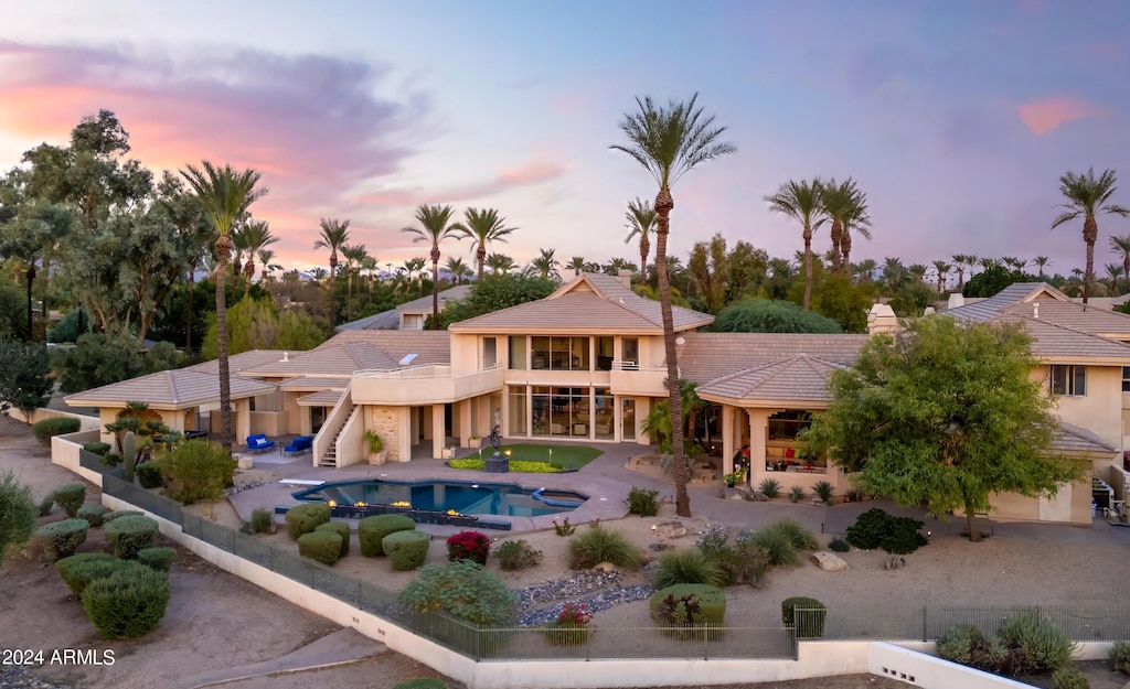 back house at dusk featuring a swimming pool with hot tub and a patio area