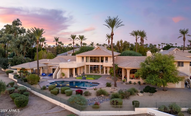 back house at dusk featuring a swimming pool with hot tub and a patio area