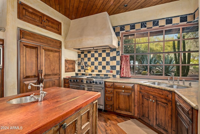 kitchen with dark hardwood / wood-style flooring, high quality appliances, tasteful backsplash, premium range hood, and sink