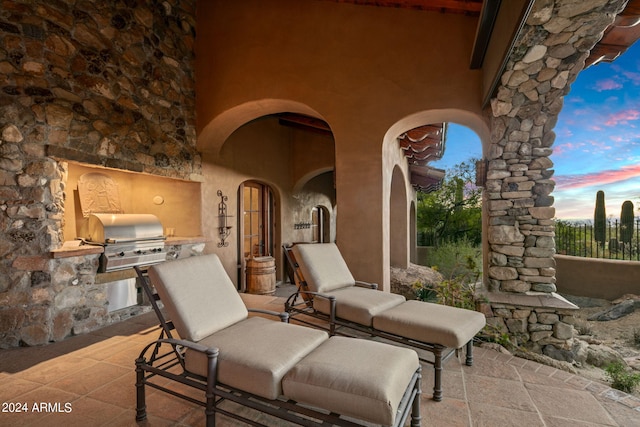 patio terrace at dusk featuring exterior kitchen and a grill