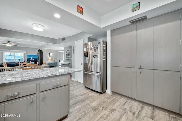 kitchen with stainless steel refrigerator with ice dispenser, ceiling fan, light stone counters, and light hardwood / wood-style flooring