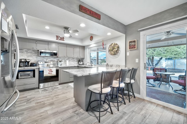 kitchen with stainless steel appliances, gray cabinetry, a kitchen breakfast bar, and kitchen peninsula