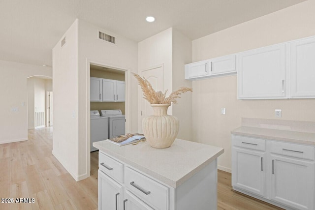 kitchen featuring visible vents, arched walkways, light wood-style flooring, washer and dryer, and white cabinetry