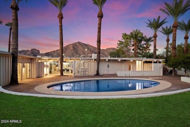 pool at dusk with a mountain view, a lawn, and a patio area