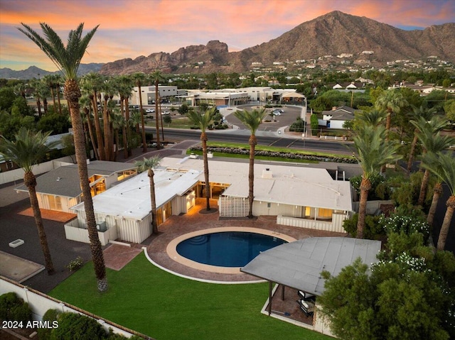 pool at dusk with a mountain view, a lawn, and a patio area