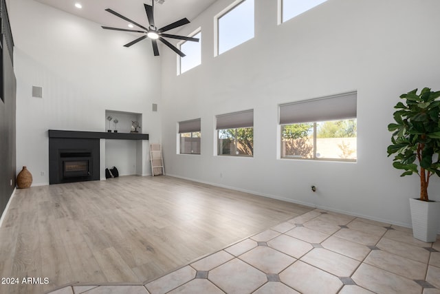 unfurnished living room with light wood-type flooring, a towering ceiling, and ceiling fan