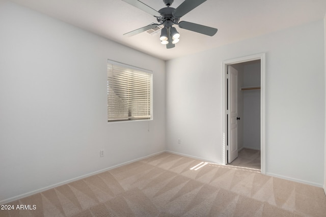 unfurnished bedroom with a walk in closet, ceiling fan, a closet, and light colored carpet