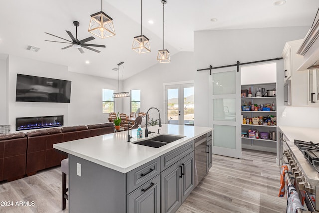 kitchen featuring gray cabinetry, sink, a barn door, light hardwood / wood-style flooring, and a kitchen island with sink