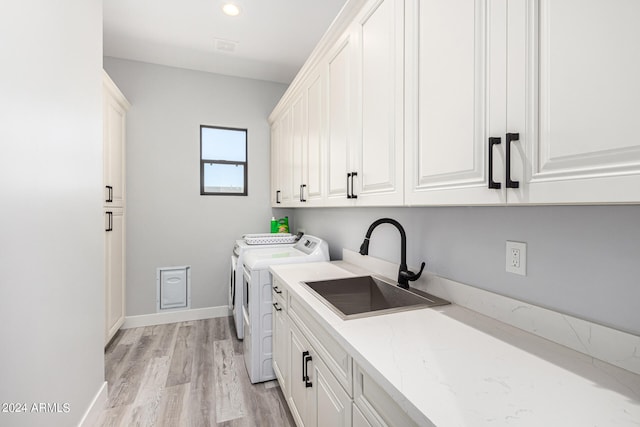 laundry room with sink, washer and clothes dryer, light wood-type flooring, and cabinets