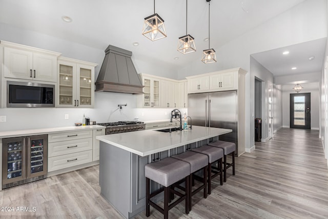 kitchen with lofted ceiling, a center island with sink, beverage cooler, premium range hood, and built in appliances