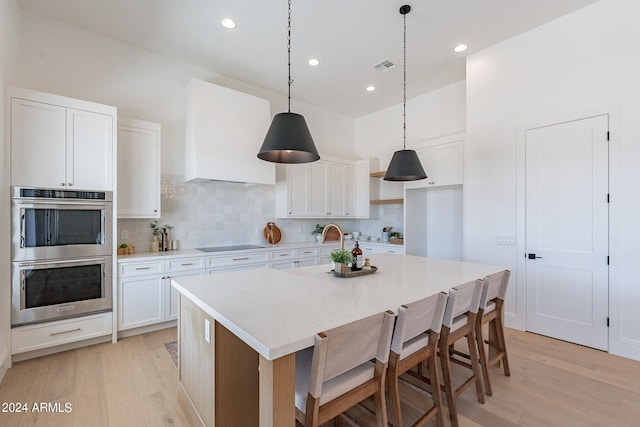 kitchen with double oven, light hardwood / wood-style flooring, tasteful backsplash, white cabinetry, and an island with sink